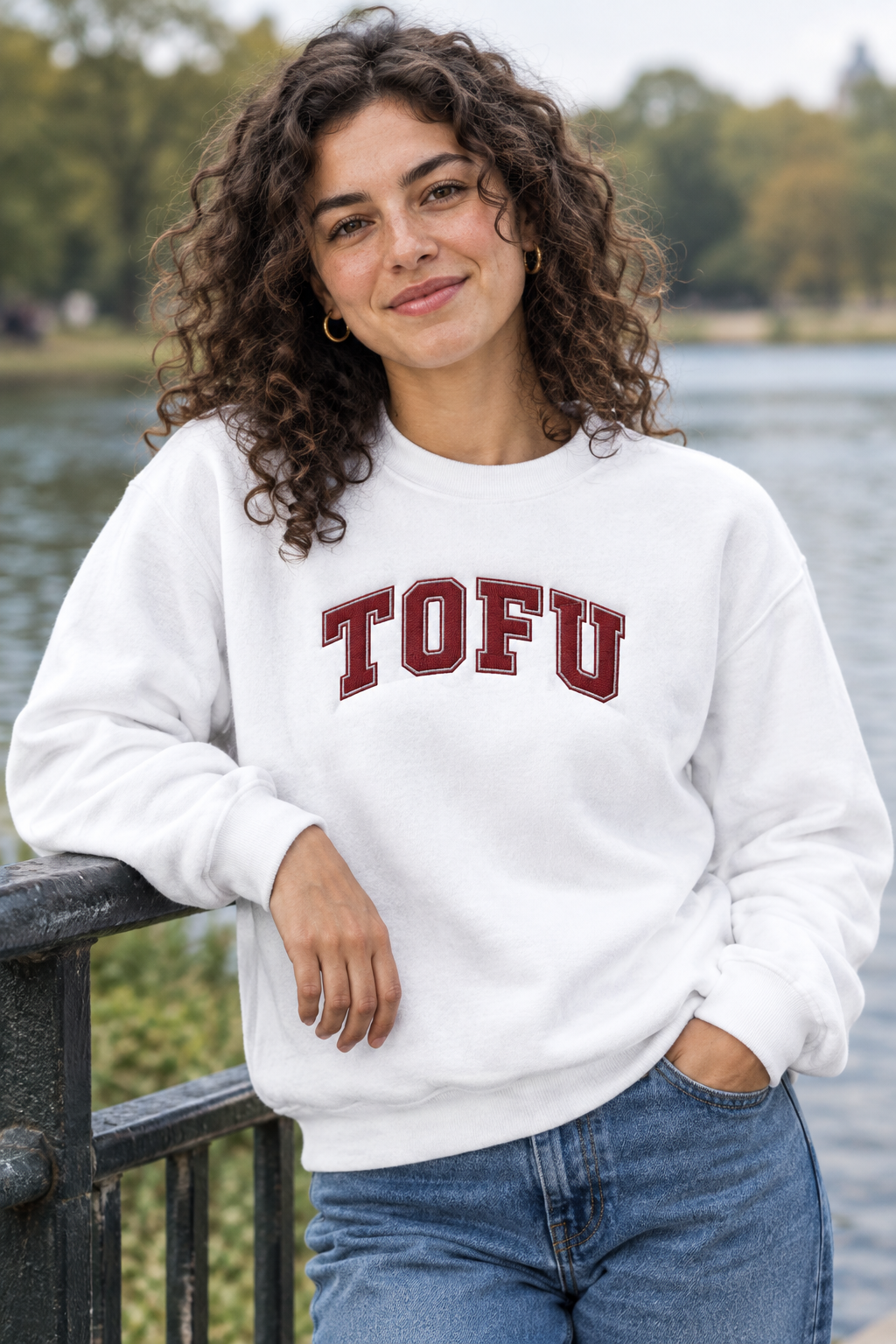 Model wearing white TOFU embroidered crewneck sweatshirt beside a lakeside railing