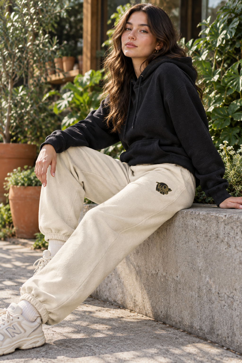 Model seated outside a plant shop wearing Dust beige vegan pig embroidered heavyweight sweatpants