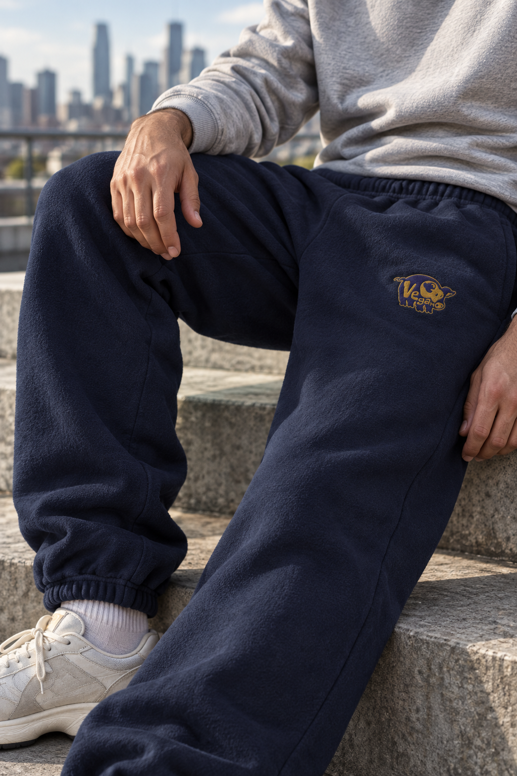 Model seated on outdoor steps wearing navy heavyweight vegan pig embroidered sweatpants