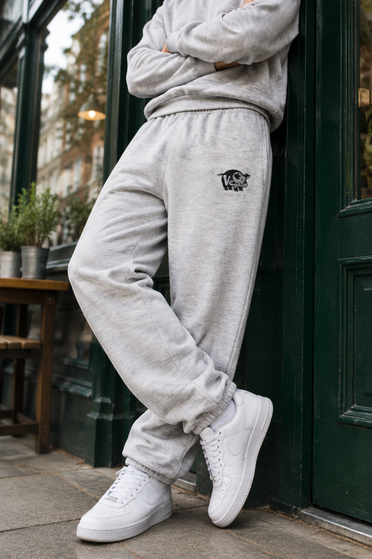 Model leaning at a green café doorway wearing Athletic Heather vegan pig embroidered heavyweight sweatpants
